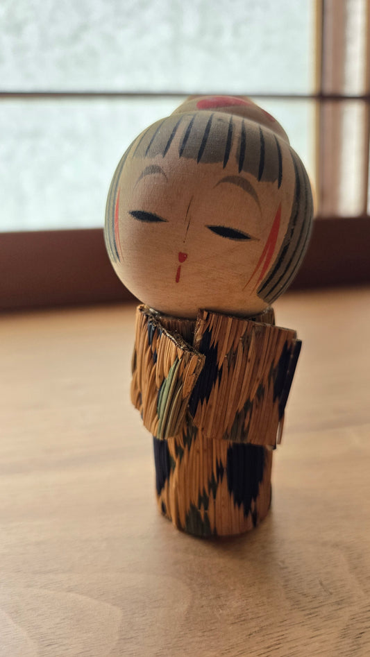 🪆 Kokeshi japonaise — Vêtement de paille tressée (mino), chevelure striée, visage aux yeux mi-clos — Vintage