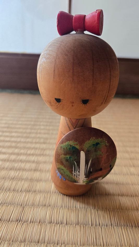 🌸 Kokeshi créative au ruban rouge et médaillon peint — paysage de cascade