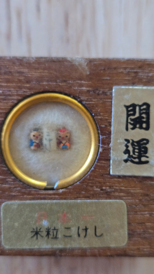 🎎 Kome-tsubu kokeshi (米粒こけし) — duo de kokeshi miniatures peintes sur grains de riz, sous loupe grossissante, boîte 3,5 cm