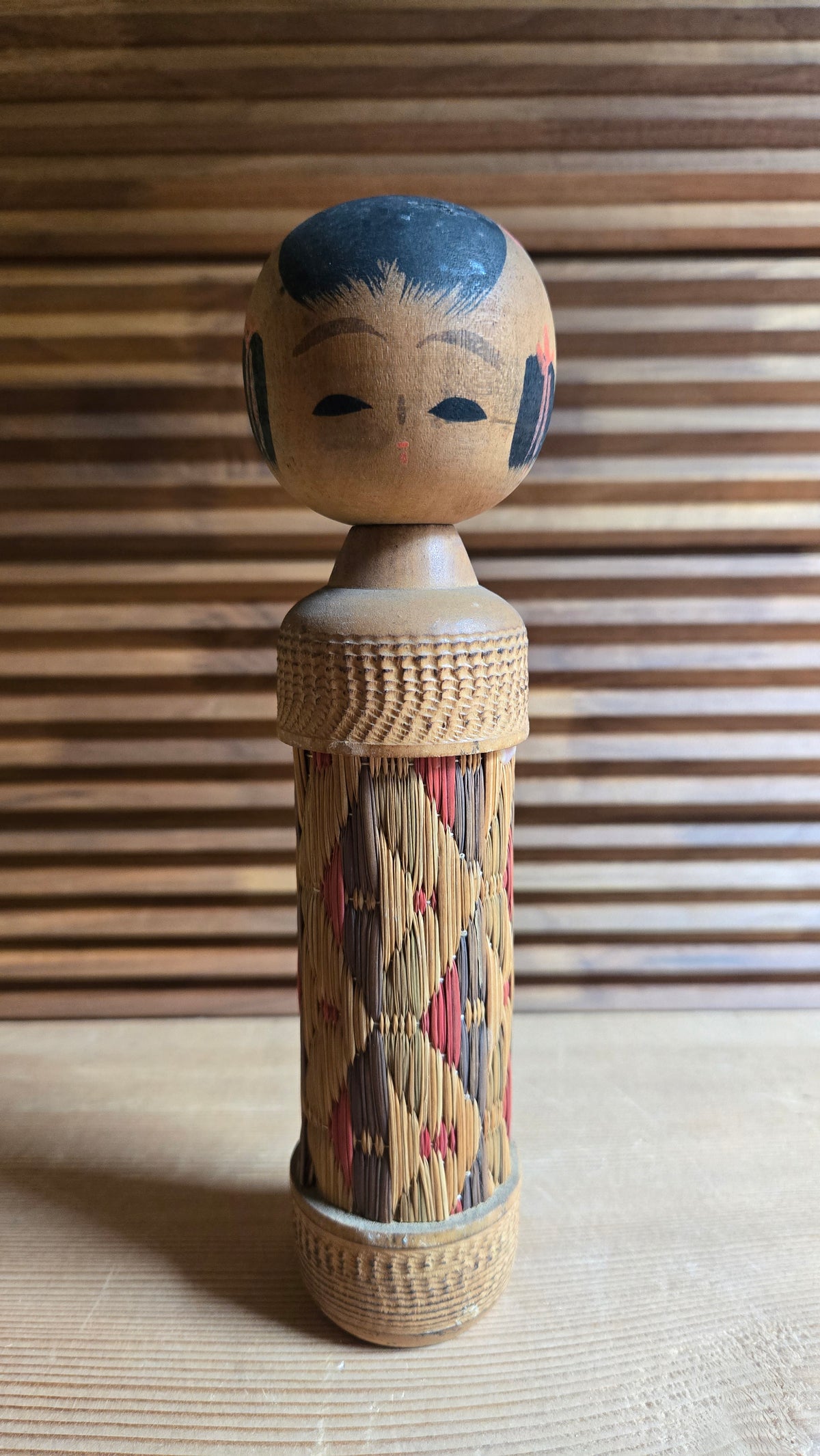 🎎 Kokeshi au corps recouvert de paille tressée, motif en losanges rouge et brun
