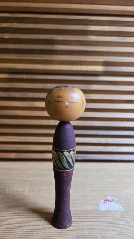 🎎 Kokeshi créative (sōsaku) en bois – corps bordeaux élancé, ceinture noire à motifs dorés, tête ronde aux yeux fermés